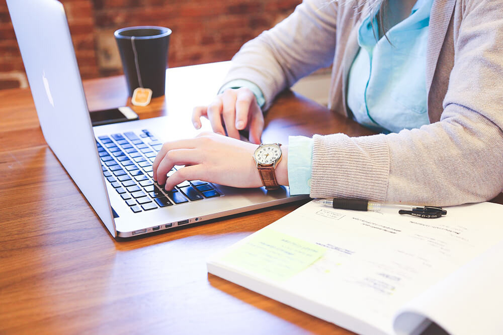 Person using laptop with book and cup of tea